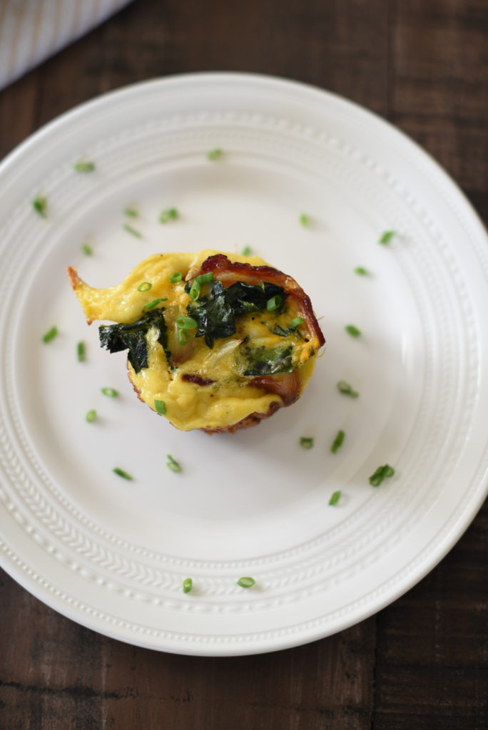 Grilled Egg Cups perfect for a summer meal prep: Light fluffy eggs, stuffed w/ greens, caramelized onions, & cheese wrapped in a piece of bacon. 