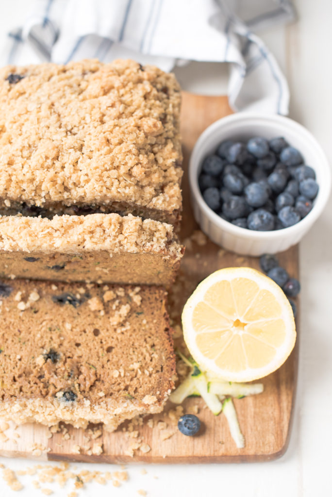 loaf of zucchini bread with oatmeal streusel on wooden cutting board with blueberries and half a lemon next to it 